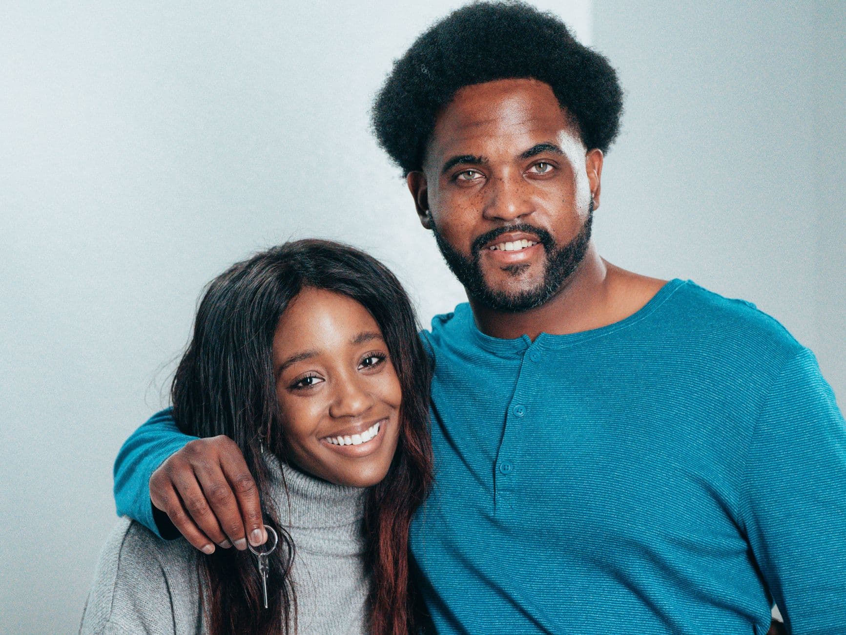A couple smiles at the camera, one of them holding a set of keys.
